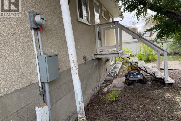 Close-up of the house exterior showing electrical meter, panel, and a weathered staircase. - 100 Marshall Crescent, Regina
