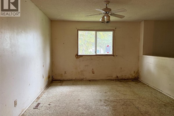 Interior view of a room with beige walls, a ceiling fan, and a large window. - 100 Marshall Crescent, Regina