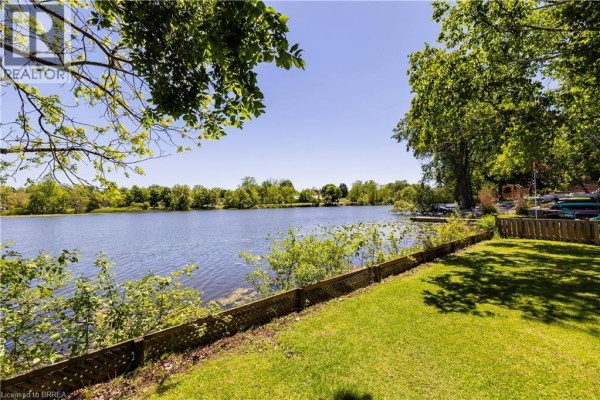 Grassy backyard with wooden fence, dock, and canoes by a lake - 100 Mechanic Street W Waterford