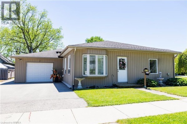 Front exterior of a beige bungalow with a white garage door, front door, and lawn. - 100 Mechanic Street W, Waterford