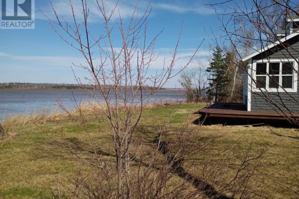 View of the house from the yard with a fire pit and colorful Adirondack chairs. - 100 Olscamp Lane, Lower Bedeque