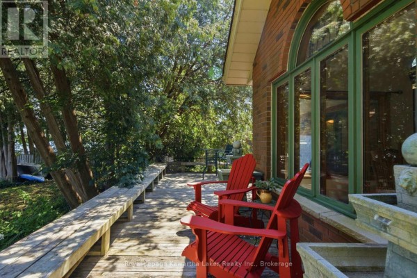 Deck with red chairs, wooden seating, and a brick house with large arched windows. - 100 Pinewood Boulevard, Kawartha Lakes