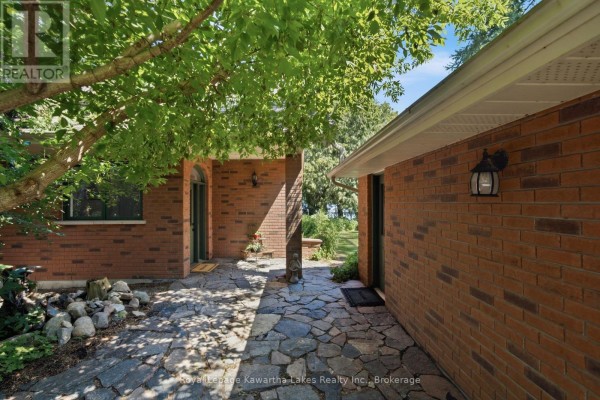 Stone pathway leading between a brick house and an attached garage with a covered entrance. - 100 Pinewood Boulevard, Kawartha Lakes