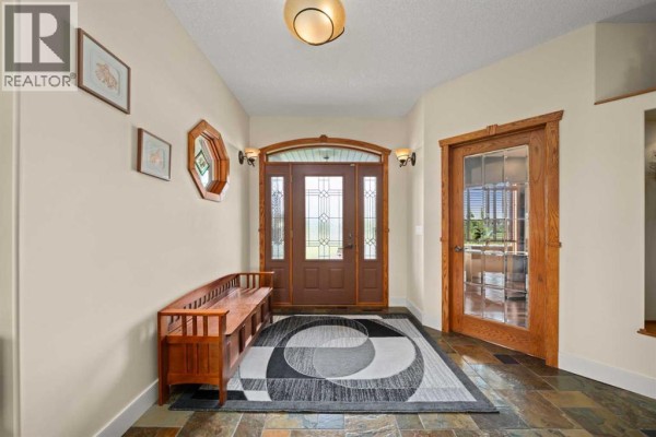 Entryway with wood bench, stained glass double front doors, and a patterned rug. - 100 Ravencrest Drive, Rural Foothills County