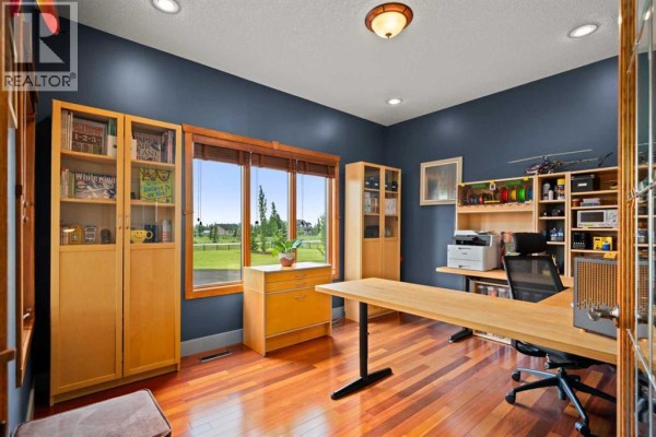 Office with dark blue walls, a large desk, bookshelves, and a window overlooking a lawn. - 100 Ravencrest Drive, Rural Foothills County