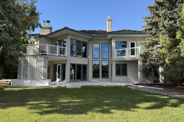 Rear exterior of a beige stucco house with multiple large windows and two balconies. - 100 Vanderbilt Drive, Winnipeg