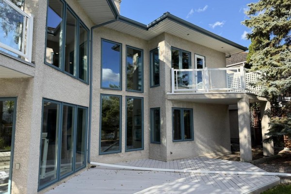 Side view of the beige stucco house rear exterior with multiple large windows and a balcony. - 100 Vanderbilt Drive, Winnipeg