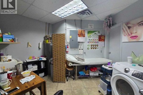 Small back room with massage table, washing machine, utility sink, and shelves. - 1000 Hamptons Drive Nw, Calgary