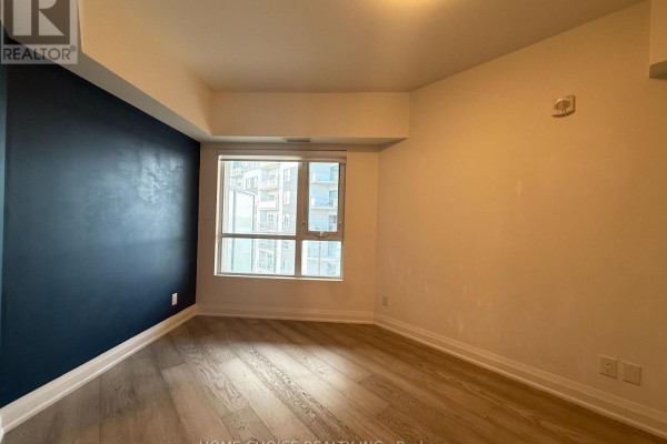 Empty room with light wood floors, a large window, and a dark blue accent wall. - 1001 - 58 Lakeside Terrace, Barrie