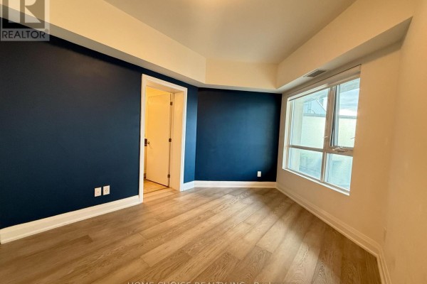 Empty room with light wood floors, large window, and a dark blue accent wall. - 1001 - 58 Lakeside Terrace, Barrie
