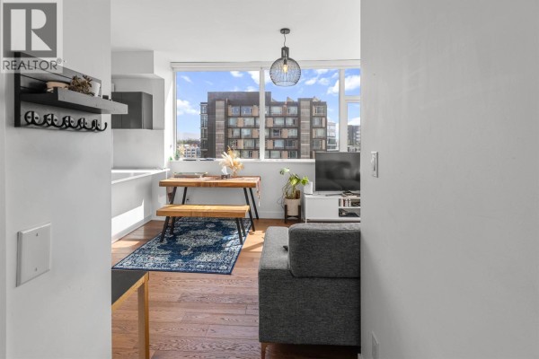 Open-concept living and kitchen area with wooden dining table, blue rug, white island, and city views. - 1001 108 E 1st Avenue, Vancouver
