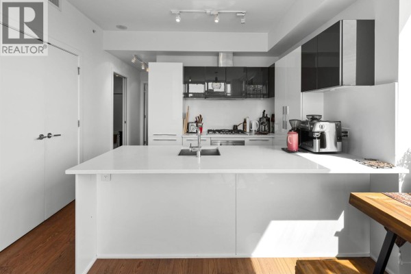 Contemporary kitchen with a long white island, stainless steel appliances, and white cabinetry. - 1001 108 E 1st Avenue, Vancouver
