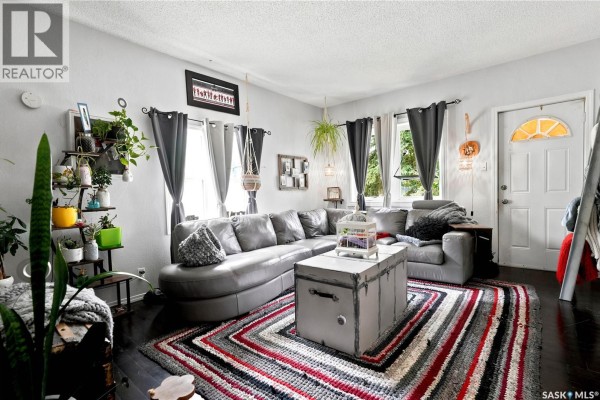 Living room with a grey sectional sofa, a striped rug, and dark wood floors. - 1001 4th Avenue Ne, Moose Jaw