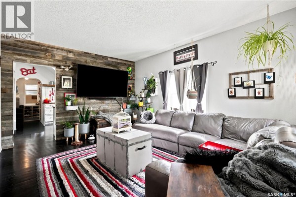 Living room with a grey sectional sofa, a rustic wood accent wall, and dark wood floors. - 1001 4th Avenue Ne, Moose Jaw