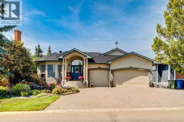 Front view of a beige stucco house with a rounded entryway, stone accents, and a paved driveway. - 1001 East Chestermere Drive, Chestermere