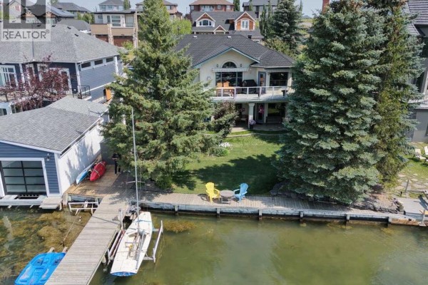 Rear view of the waterfront house with a large deck overlooking the lake and a wooden dock. - 1001 East Chestermere Drive, Chestermere