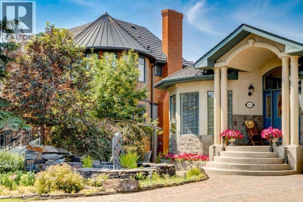 Close-up of the house entrance with a blue door, stone facade, and landscaping with pink flowers. - 1001 East Chestermere Drive, Chestermere