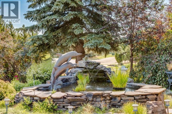 A tiered stone fountain with dolphin sculptures and running water in a landscaped garden setting. - 1001 East Chestermere Drive, Chestermere