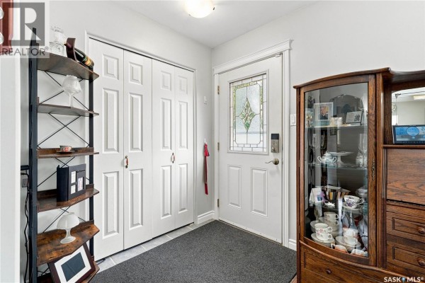 Interior view of the front entryway with white double doors, a glass paneled front door, and a display cabinet. - 1001 Mahoney Avenue, Saskatoon