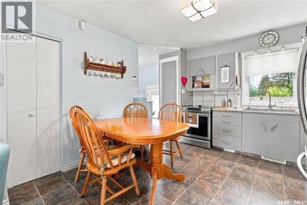 Kitchen and dining area with a wooden table and chairs, grey cabinets, stainless steel appliances, and tile flooring. - 1001 Mahoney Avenue, Saskatoon