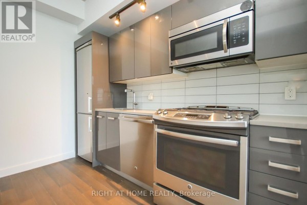 Close-up view of a modern kitchen with grey cabinets, stainless steel appliances, and a white tile backsplash. - 1002 - 224 Lyon Street, Ottawa