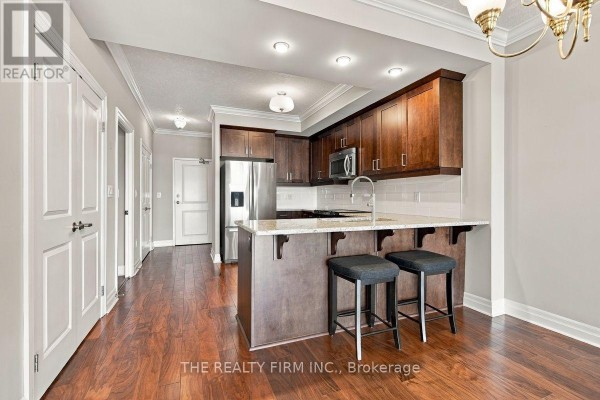 Kitchen area with dark wood cabinets, granite countertops, stainless steel appliances, and a breakfast bar. - 1002 - 240 Villagewalk Boulevard, London North