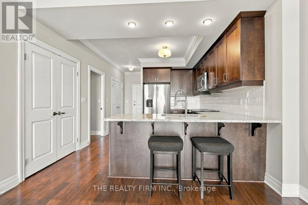Kitchen area with dark wood cabinets, granite countertops, stainless steel appliances, and a breakfast bar. - 1002 - 240 Villagewalk Boulevard, London North