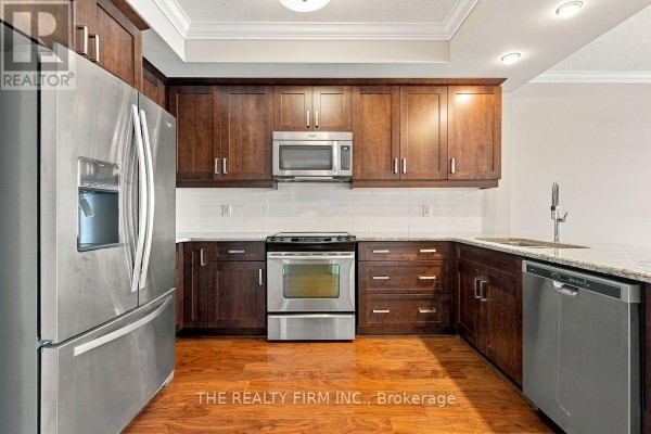 Corner kitchen with dark wood cabinets, stainless steel appliances including a refrigerator, stove, and dishwasher. - 1002 - 240 Villagewalk Boulevard, London North