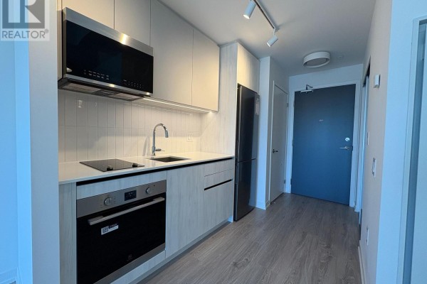 Compact apartment kitchen with light wood cabinets, white quartz counters, and stainless steel appliances. - 1002 - 2485 Eglinton Avenue W, Mississauga
