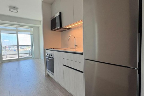 View of the apartment kitchen and living area with a large window and light wood flooring. - 1002 - 2485 Eglinton Avenue W, Mississauga