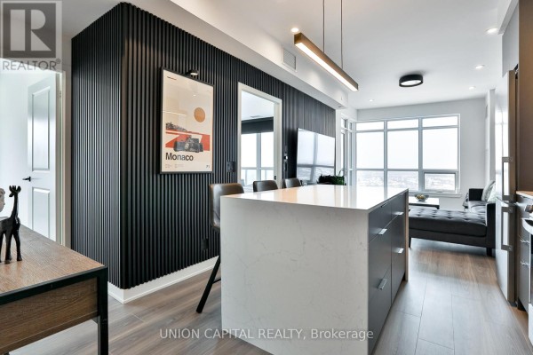 Open concept living area with a large island, textured black wall, and view through window. - 1002 - 30 Upper Mall Way, Vaughan