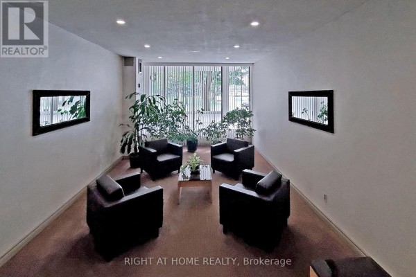 A small seating area with four black armchairs, a glass coffee table, and plants by a large window. - 1002 - 40 Bay Mills Boulevard, Toronto