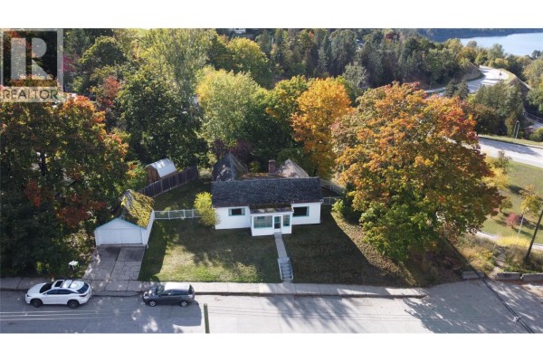 Aerial view of a small white house with a driveway, garage, and trees on a street. - 1002 Kootenay Street, Nelson