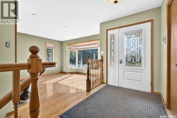 Entrance foyer with wood railings, white double doors with decorative glass, and light green walls. - 1002 Vaughan Street, Moose Jaw