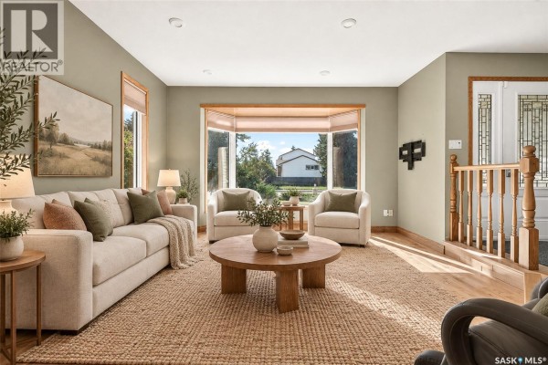 Living room with a sofa, two armchairs, round wooden coffee table, and a large bay window. - 1002 Vaughan Street, Moose Jaw