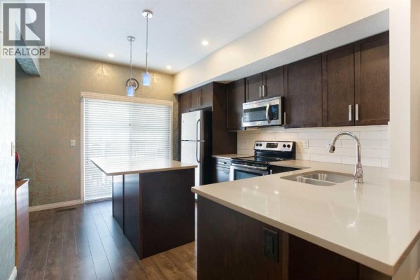 Modern kitchen with dark brown cabinets, stainless steel appliances, white quartz countertops, and a central island. - 1003, 280 Williamstown Close Nw, Airdrie