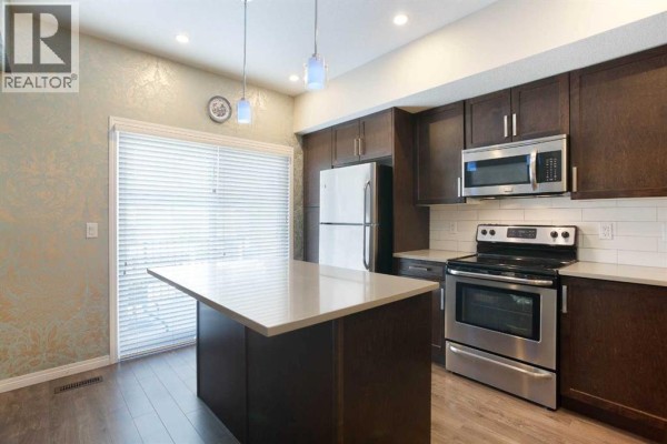 Kitchen with dark brown cabinets, stainless steel appliances, white quartz countertops, and a view of the living area. - 1003, 280 Williamstown Close Nw, Airdrie