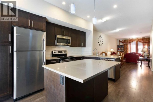 Open-concept kitchen and living room with dark cabinets, stainless steel appliances, and a large window. - 1003, 280 Williamstown Close Nw, Airdrie