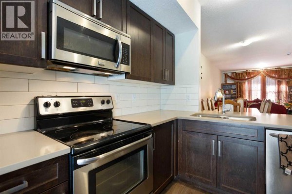 Close-up of the kitchen featuring dark cabinets, white subway tile backsplash, stainless steel stove, and quartz countertops. - 1003, 280 Williamstown Close Nw, Airdrie
