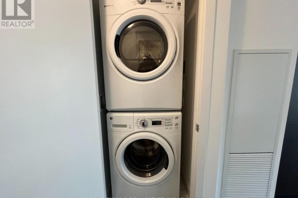 Stacked white washer and dryer unit inside a closet next to a grey panel. - 1003 - 38 Iannuzzi Street, Toronto