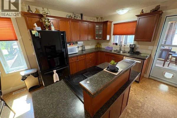 Kitchen with dark wood cabinets, black appliances, granite countertops, and a central island with a stovetop. - 10032 102 Street, Peace River