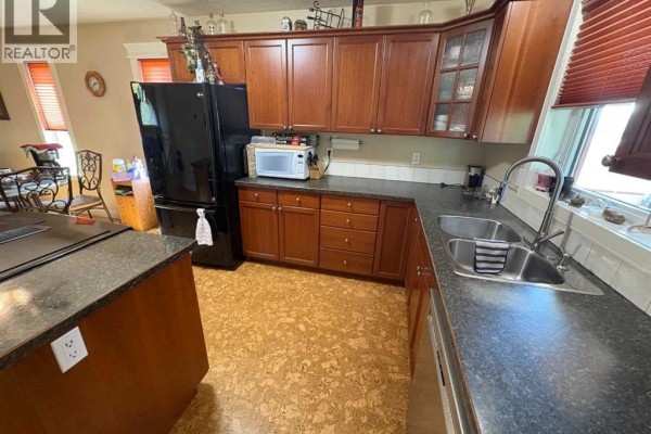 View of the kitchen sink and countertops, with dark wood cabinets above and cork flooring below. - 10032 102 Street, Peace River