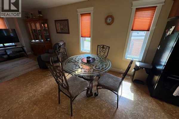 Dining area with a glass-top table, four ornate chairs, and two windows with orange blinds. - 10032 102 Street, Peace River