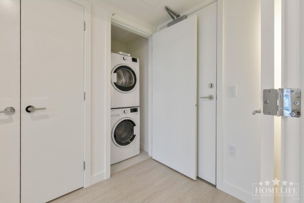 Compact laundry closet with stacked white washer and dryer units. - 1004 13675 107a Avenue, Surrey