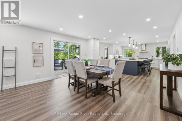 Living room with a bay window, sectional sofa, coffee table, and open view to dining area. - 1004 Telecom Road, Kawartha Lakes