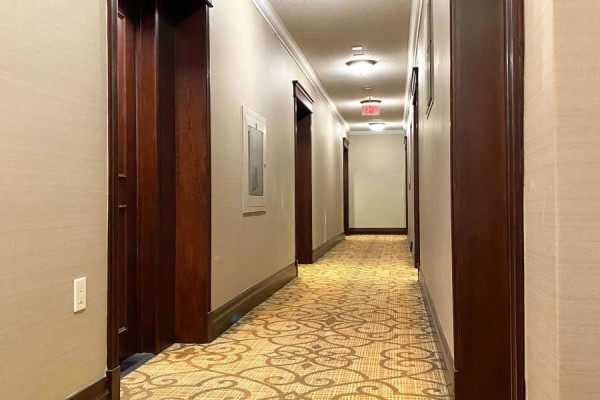 A long hallway with beige wallpaper, patterned carpet, and dark wood trim leads to doorways. - 1005 - 1 Clairtrell Road, Toronto
