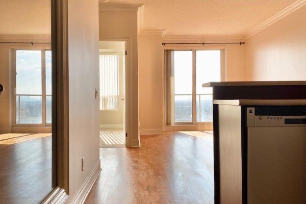 View from a doorway into a living area with wooden floors and large windows overlooking the city. - 1005 - 1 Clairtrell Road, Toronto
