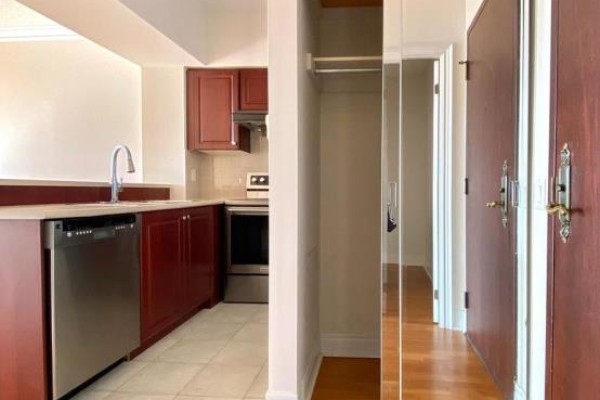 A kitchen with dark red cabinets, stainless steel appliances, and a mirrored closet door nearby. - 1005 - 1 Clairtrell Road, Toronto