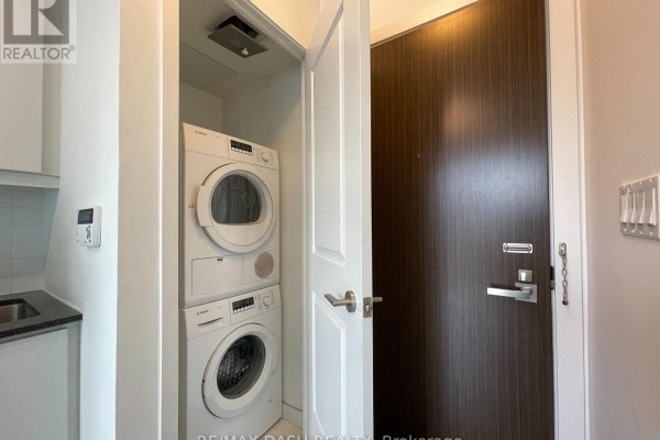 Closet with stacked Bosch washer and dryer next to a dark wood entry door. - 1005 - 1 The Esplanade Drive, Toronto