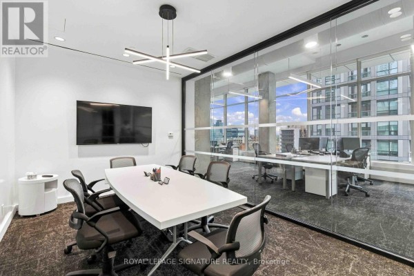 Conference room with a white table, black chairs, large TV, and glass walls overlooking the office. - 1005 - 130 Queens Quay E, Toronto